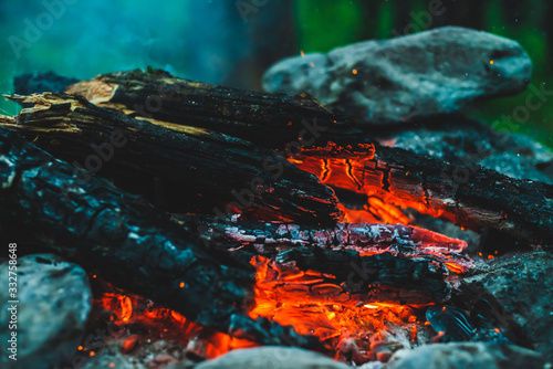 Vivid smoldered firewoods burned in fire close-up. Atmospheric warm background with orange flame of campfire and blue smoke. Unimaginable full frame image of bonfire. Burning logs in beautiful fire.