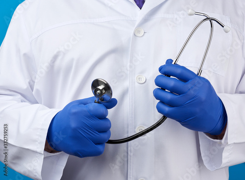 adult male doctor in a white medical coat stands and holds a black stethoscope on a blue background