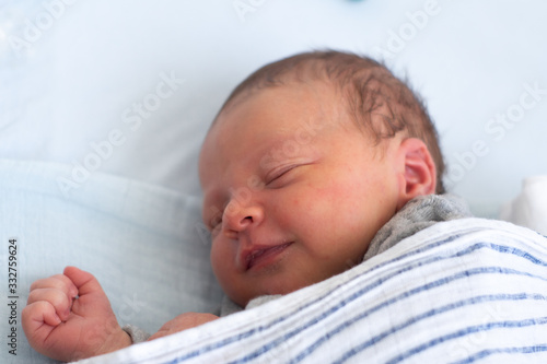 Happy smiling newborn baby boy sleeping in baby bed under striped blanket. Sweet dreams of a cheerful new born.