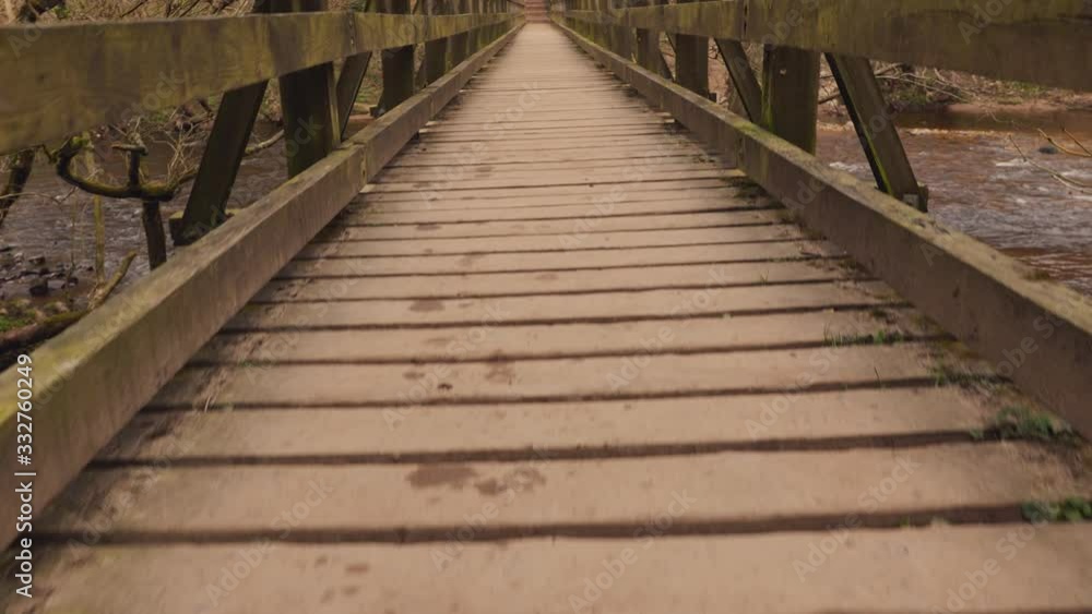 A first person view of someone walking across a wooden footbridge over a river in the forest A first person view of someone walking across a wooden footbridge over a river in the forest