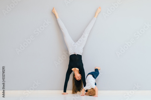 Fotografia Sportive brunette mother with baby son doing press exercise on grey yoga mat over gray wall background