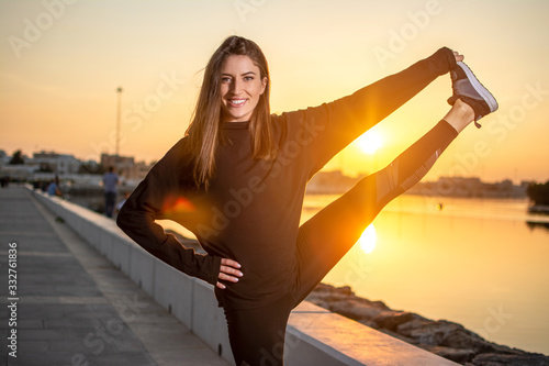 Young sportswoman raising her leg and holding it by hand in balance pose, while practicing yoga outdoors