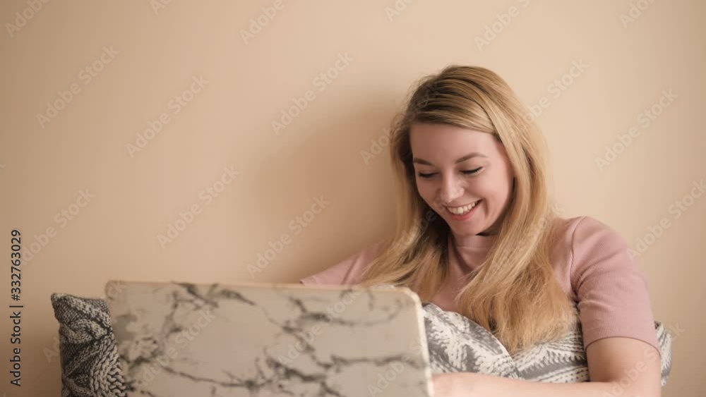 A young woman works at a computer at home in bed, conducts correspondence, smiles and laughs A young woman works at a computer at home in bed, conducts correspondence, smiles and laughs