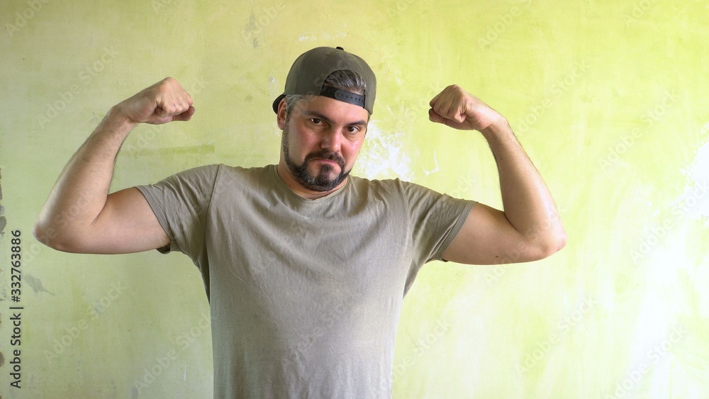 Naklejka premium A man by the wall shows biceps. Athlete in the gym. Sportsman. Healthy lifestyle.