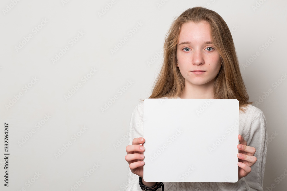Positive girl holds a blank poster for text. Schoolgirl with a smile holds a white sheet for text. Positive girl holds a blank poster for text. Schoolgirl with a smile holds a white sheet for text.