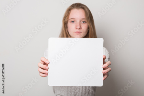 Positive girl holds a blank poster for text. Schoolgirl with a smile holds a white sheet for text.