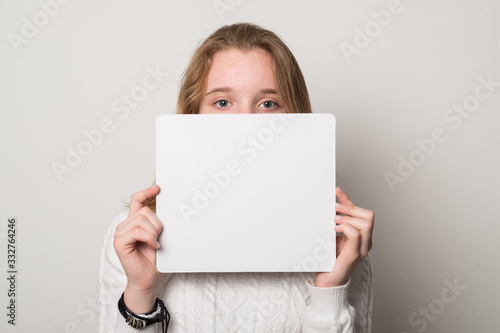 Positive girl holds a blank poster for text. Schoolgirl with a smile holds a white sheet for text.