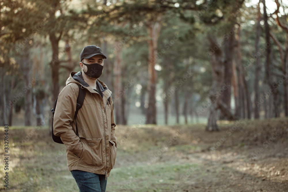 man in medical mask walks through park. Man with backpack in jacket and cap man in medical mask walks through park. Man with backpack in jacket and cap