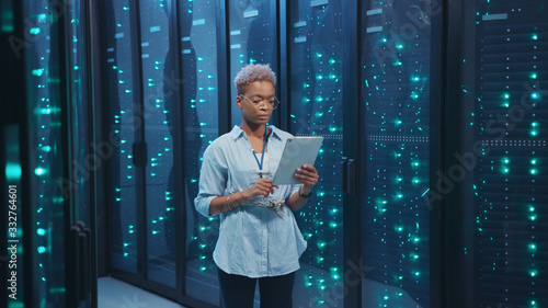 Картината върху платно Afro-american female IT administrator walking in server corridor diagnosing hardware system performance in data center cyber secure storage