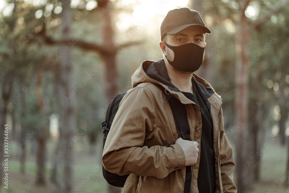 Walking man in black medical mask. Man walks through the park with a backpack. Walking man in black medical mask. Man walks through the park with a backpack.