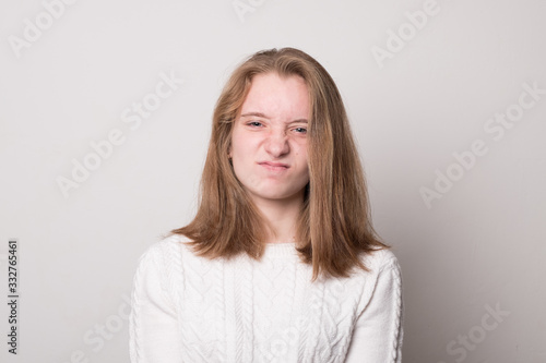 Emotional teen girl grimaces. Studio image of a cute smiling young girl on a gray background.