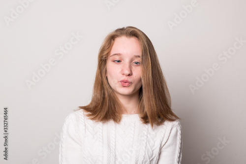 Emotional teen girl grimaces. Studio image of a cute smiling young girl on a gray background.