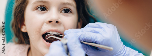 Teeth examination procedure done by a dentist to a small caucasian girl with opened mouth photo