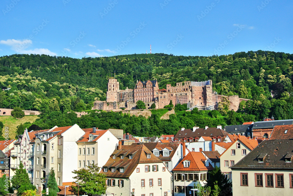 Heidelberg, Germany - panorama of the city, houses with brown roofs over which the Heidelberg castle on the northern green slope of the Konigstuhl mountain, blue sky in the summer afternoon.