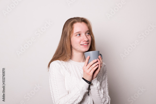 Positive girl holds a mug of tea. Teen girl drinks from a mug.