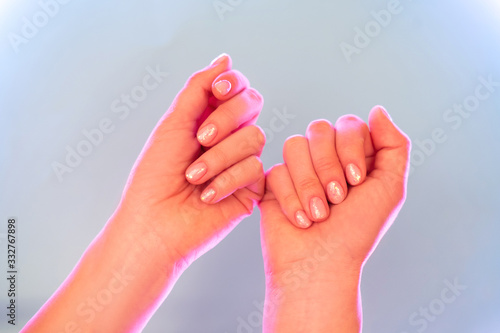 Female hands with perfect manicure in trendy neon light on grey background. Beauty concept.