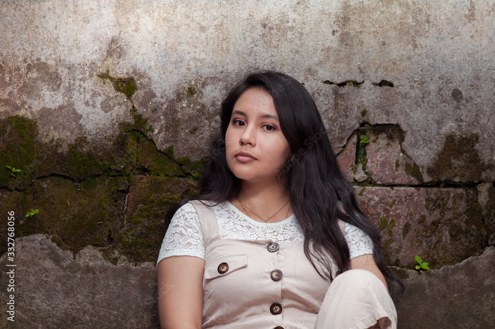 Portrait of young woman sitting and leaning against an old wall Portrait of young woman sitting and leaning against an old wall