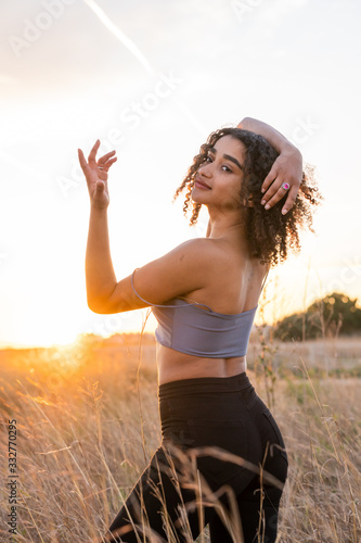 Fototapeta Naklejka Na Ścianę i Meble -  African American young woman with curly black hair dancing in the field