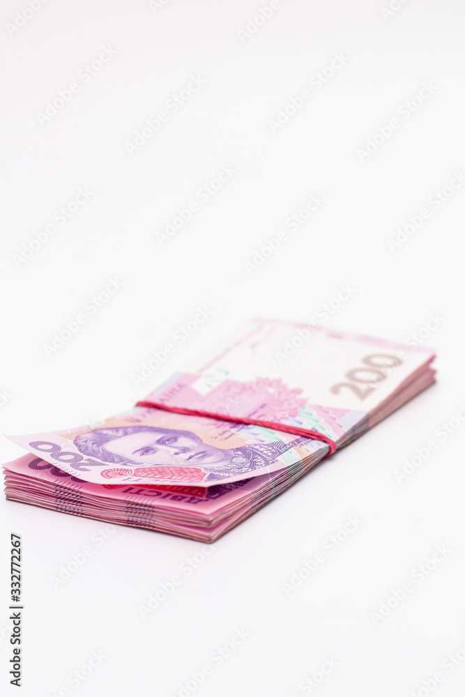 A lot of new banknotes in denominations of 200 Ukrainian hryvnias bandaged with an elastic band isolated on a white background with shadow. European money exchange. Ukraine currency. Selective focus A lot of new banknotes in denominations of 200 Ukrainian hryvnias bandaged with an elastic band isolated on a white background with shadow. European money exchange. Ukraine currency. Selective focus