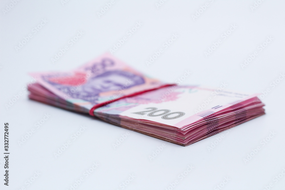 A lot of new banknotes in denominations of 200 Ukrainian hryvnias bandaged with an elastic band isolated on a white background with shadow. European money exchange. Ukraine currency. Selective focus A lot of new banknotes in denominations of 200 Ukrainian hryvnias bandaged with an elastic band isolated on a white background with shadow. European money exchange. Ukraine currency. Selective focus