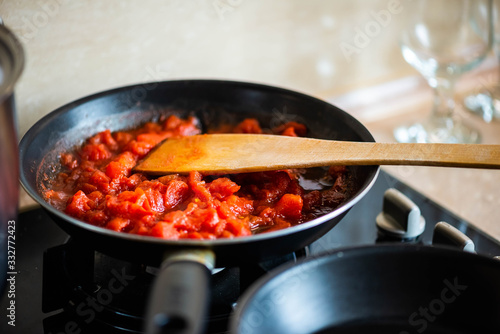 Tomato sauce with cut tomatoes, with wooden spatula in the pan. On the dark glass cooker. Food preparation background