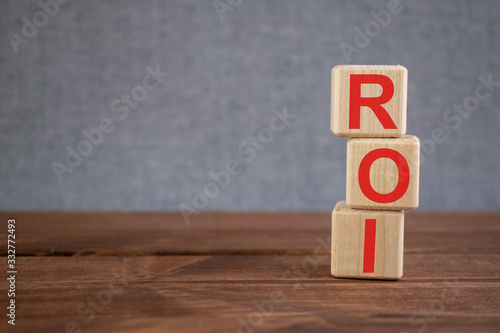 ROI (Return On investment) acronym on wooden cubes on dark wooden backround. Business management, Stocks investment concept.