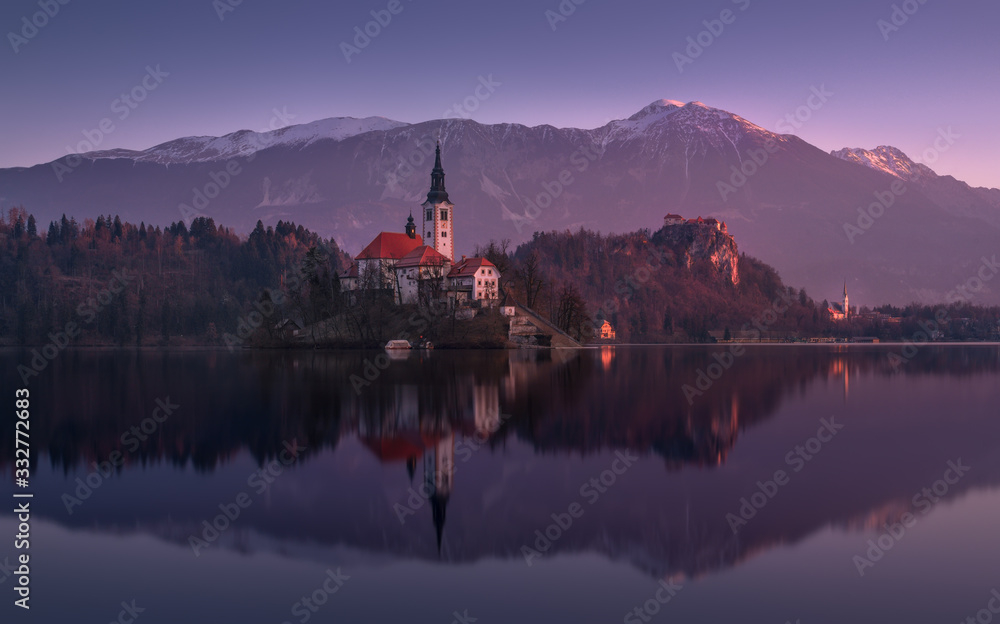 Beginning Of The Day At Lake Bled In Winter, Slovenia. Pinky Sunrise With Perfect Reflection Of Julian Alps And St. Marys Church Of The Assumption.Slovinian Landscape With Bled Castle ( Blejski grad )