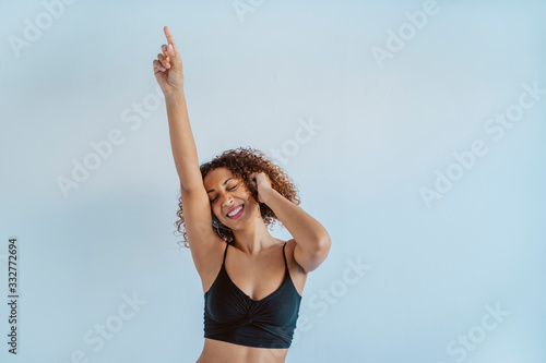 Young afro cheerful woman dancing to the beat and rhythm of black music. Afro culture lifestyle with technology at home. Fit african american dancer listening to music with wireless headphones.