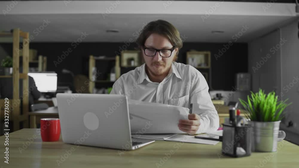 Young manager is watching documents sitting at desk in office Young manager is watching documents sitting at desk in office