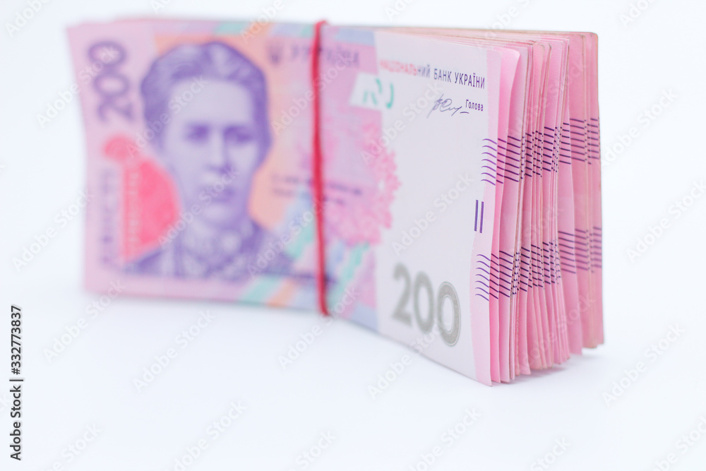 A lot of new banknotes in denominations of 200 Ukrainian hryvnias bandaged with an elastic band isolated on a white background with shadow. European money exchange. Ukraine currency. Selective focus A lot of new banknotes in denominations of 200 Ukrainian hryvnias bandaged with an elastic band isolated on a white background with shadow. European money exchange. Ukraine currency. Selective focus