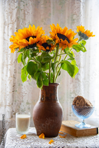 Vintage still life . A bouquet of sunflowers in a vintage clay jug, cookies and milk, a yellowed book on a lace tablecloth by the window.