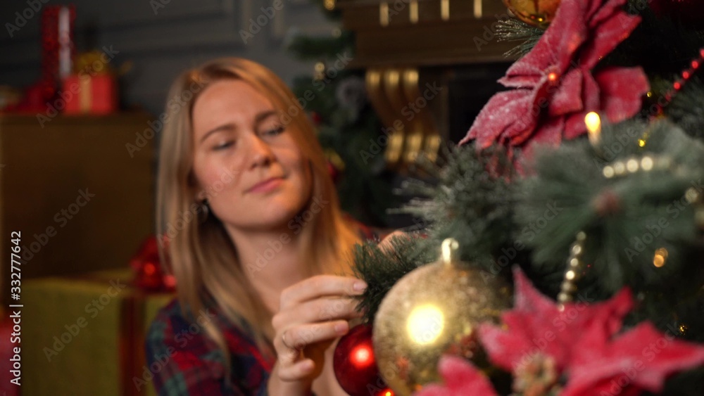 Young beautiful girl or woman in a red plaid shirt decorates a Christmas tree for Christmas or New Year. Young beautiful girl or woman in a red plaid shirt decorates a Christmas tree for Christmas or New Year.