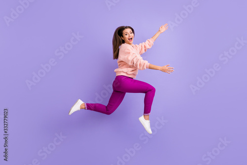 Full length profile photo of cheerful lady jumping high rushing friends meeting raise hands to empty space wear casual fluffy pullover pants shoes isolated purple color background