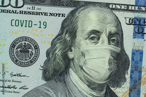 Medical mask on a banknote of 100 dollars, concept of the global financial crisis. Medical mask or surgical mask on american money. COVID-19 coronavirus in USA. Doctor mask protects against COVID-19.