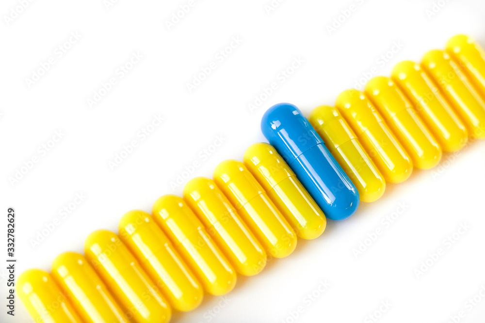 yellow capsules on a white background laid out in a row and blue which stands out. The other's concept. yellow capsules on a white background laid out in a row and blue which stands out. The other's concept.