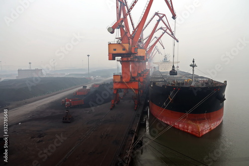Cargo terminal for discharging coal cargos by shore cranes during foggy weather. Port Bayuquan,China. January, 2020.