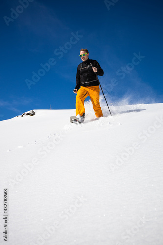 Winter sports - young man running with snowshoes downhill in high mountains covered with lots of snow