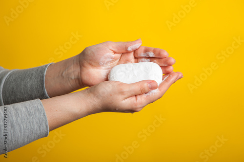 female hands holding a piece of white soap on a yellow studio background. Bright close-up photo.