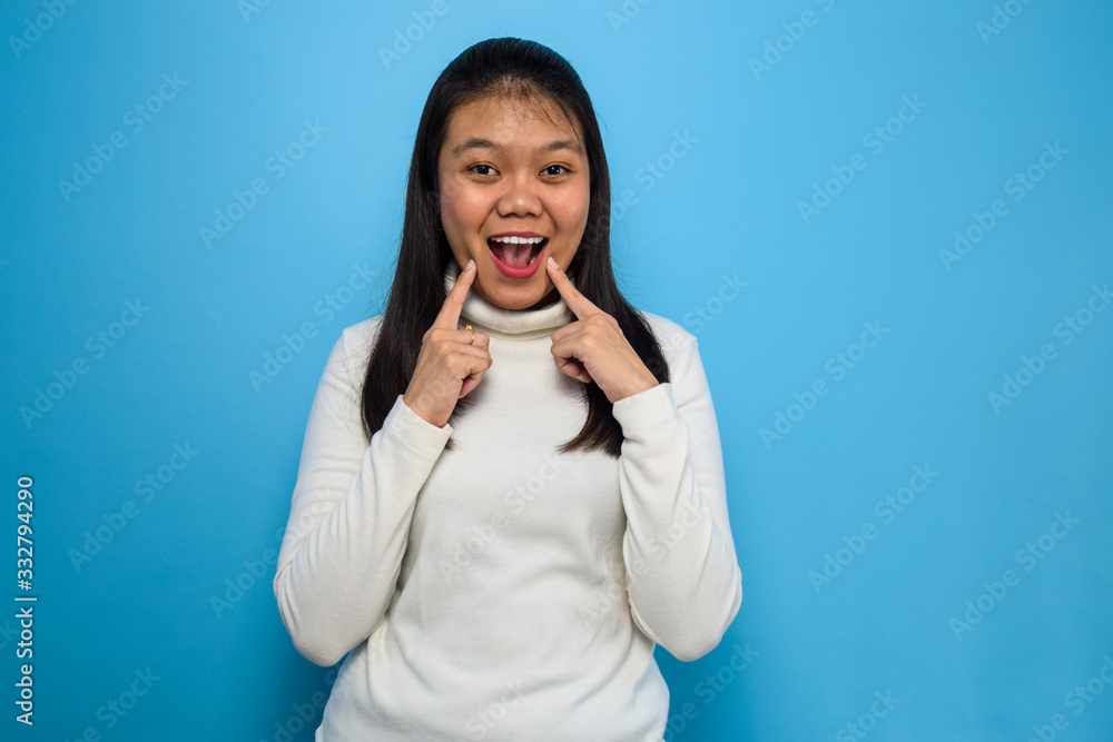 Portrait of Young beautiful asian women using white T-shirt with blue isolated background, fingers pointing and forcing cheerful smile Portrait of Young beautiful asian women using white T-shirt with blue isolated background, fingers pointing and forcing cheerful smile