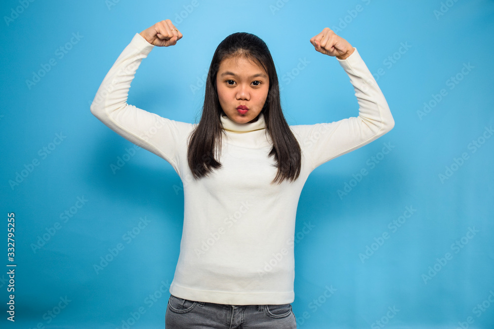 Fototapeta premium Portrait of Young beautiful asian women using white T-shirt with blue isolated background, raises arms and shows biceps
