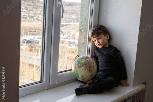 a bored lonely child with a globe in his hands during the quarantine of the epidemic, Kovid-19 looks out the window and dreams of going outside.