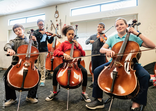 Teenage girls and boys playing cellos and violins in classroom photo