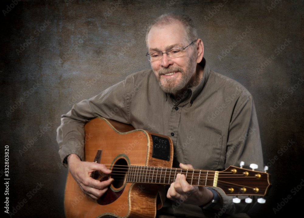 Obraz premium Mature man with full beard and thinning gray hair playing six string acoustic guitar texture background