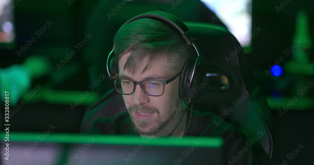 Man with a beard and glasses working at a computer, talking on a microphone. Man plays an online game, communicates with players. Portrait view. Man with a beard and glasses working at a computer, talking on a microphone. Man plays an online game, communicates with players. Portrait view.