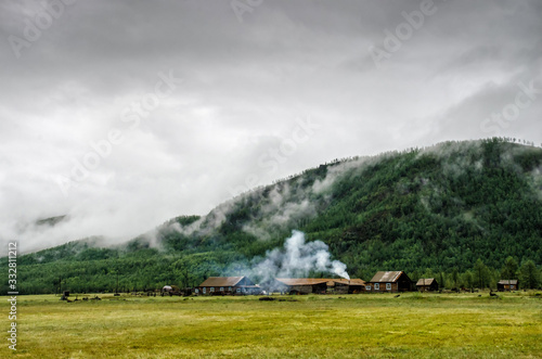 Old wooden houses in the village with smoke from chimneys near the misty mountain