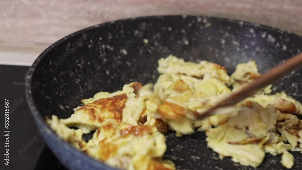 Scrambled eggs browning in black skillet with wood spatula, close up Scrambled eggs browning in black skillet with wood spatula, close up