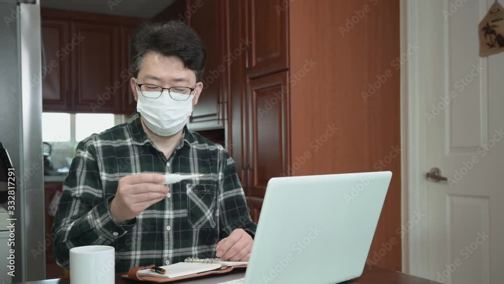 An Asian businessman is self-isolated and working from home because of a massive pandemic. A man holding a thermometer to measure body temperature.