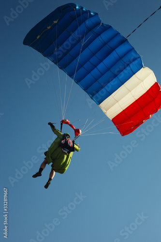 Skydiver in wingsuit under a canopy of a parachute close-up against a blue sky. Parachute jumping.