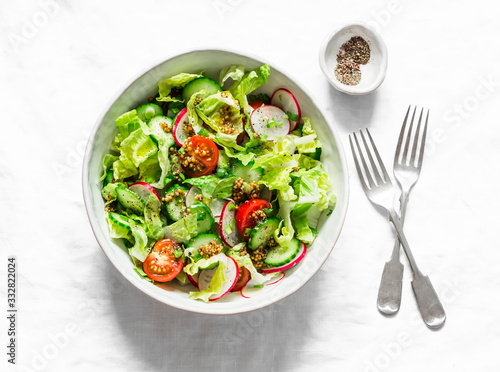 Easy vegetarian vegetable salad with fresh vegetables. Cherry tomatoes , romano lettuce, cucumbers, radishes and french mustard, olive oil, lemon salad dressing on a light background, top view