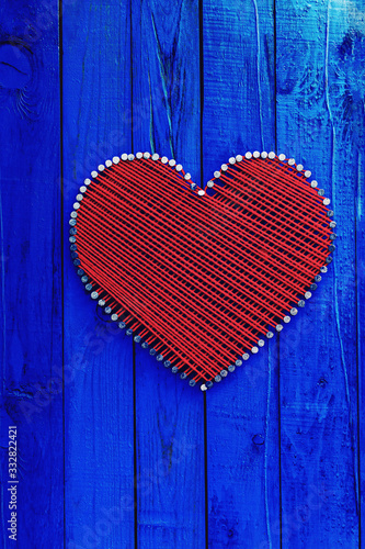 Antique blue wood sign with red and white hearts on burlap background hanging by braided rope on aged wooden fence